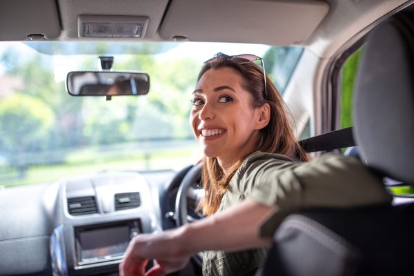 Pretty young woman driving in reverse looking back over shoulder smiling.