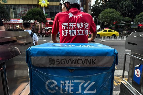 重慶街頭一名身穿京東到家（JD Daojia）制服、騎著電動車的外賣員，車上卻載著一個餓了麼（Ele.me）的保溫外送箱，在紅燈前等候過馬路。（Cheng Xin/Getty Images）
