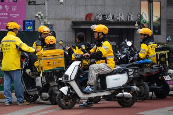 一群身穿黃色頭盔和制服的美團外賣員，2025年3月22日聚集在重慶的一間飯店外。（Cheng Xin/Getty Images）