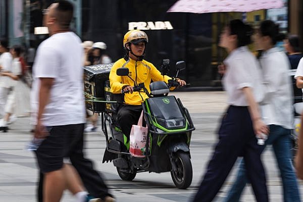 重慶一名身穿黃色制服、戴著頭盔的美團外賣員。（ Cheng Xin/Getty Images）