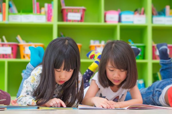Two girl kid lay down on floor and reading tale book  in preschool library,Kindergarten school education concept